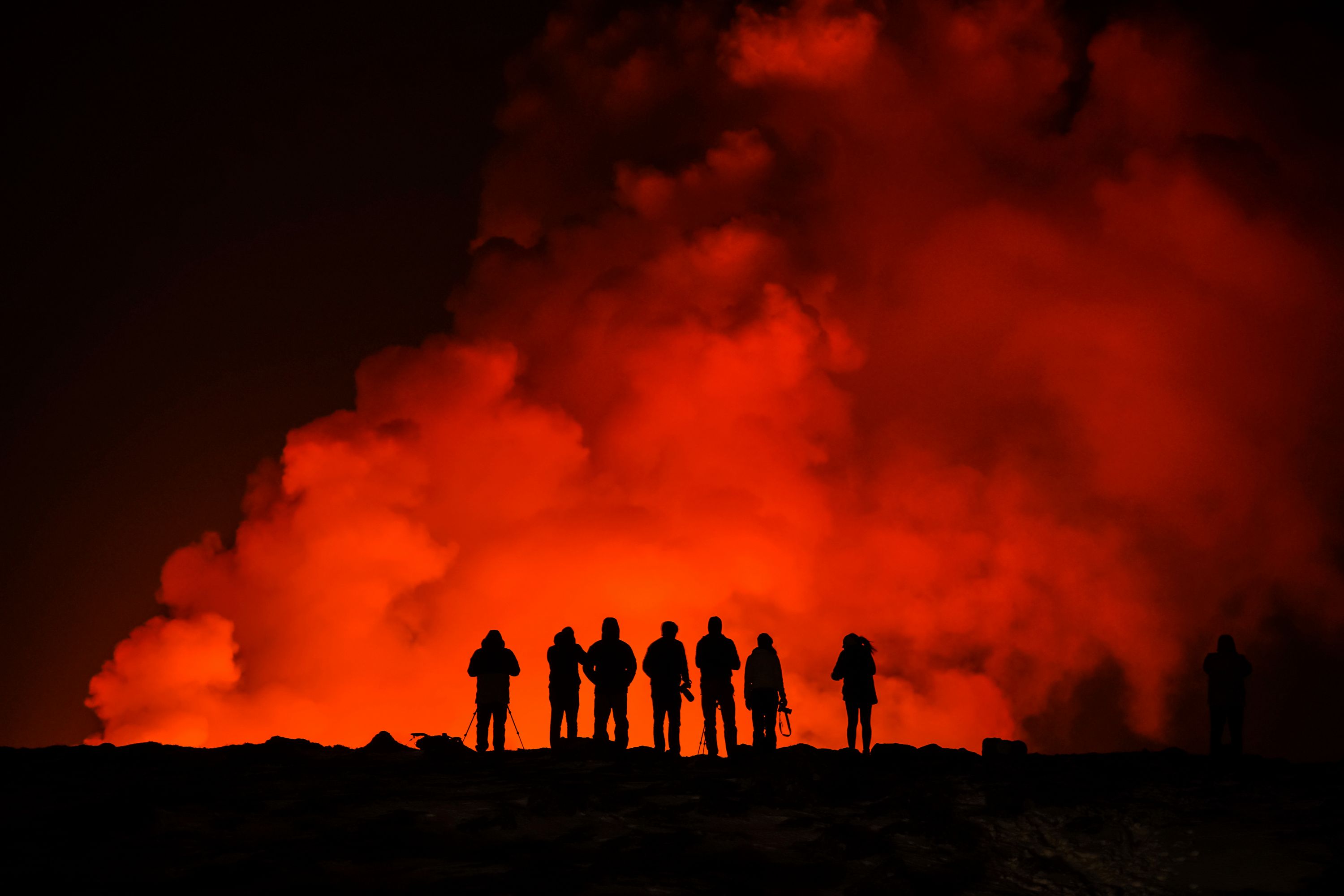 Flere personer ser på torsdagens utbrudd. Islands beliggenhet gjør at landet har et ekstremt høyt nivå av geologisk aktivitet. De fleste utbruddene er små og gir ikke store konsekvenser for dem som bor der. Foto: Marco Di Marco / AP / NTB