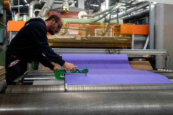 En fabrikkarbeider sjekker kvaliteten på underlaget som skal legges på løpebanen i Paris-OL. Foto: Luca Bruno / AP / NTB