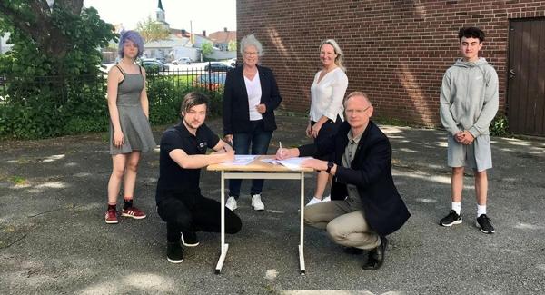 Prosjektdirektør i AF Bygg Thomas Nordenhaug og kommunedirektør Roar Vevelstad signerer kontrakten. Bak fra venstre nestleder i elevrådet Emma Midtfjell, ordfører Anne-Kari Holm, styreleder i Halden idrettsråd Torhild G. Huseby og elevrådsleder Daniel Dahl Bjørneby. Foto: Henrik D. Meyer/Halden kommune