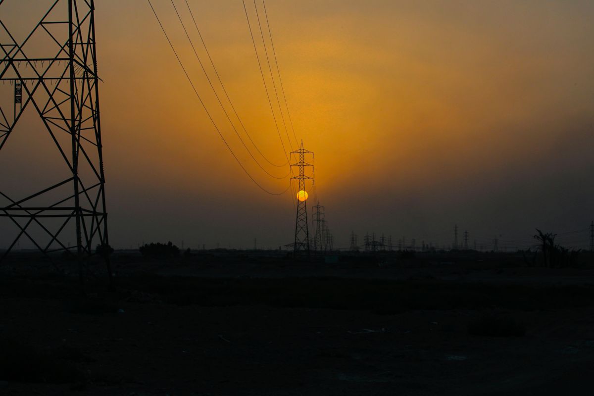 Solen går ned over kraftlinjene ved den irakiske byen Basra, som fører iransk strøm inn i Irak. Irak forsøker nå å bøte på kraftunderskuddet ved å bygge en rekke solkraftanlegg, og torsdag ble det kjent at et norskledet konsortium skal bygge to av dem. Foto: Nabil al-Jurani / AP Photo / NTB