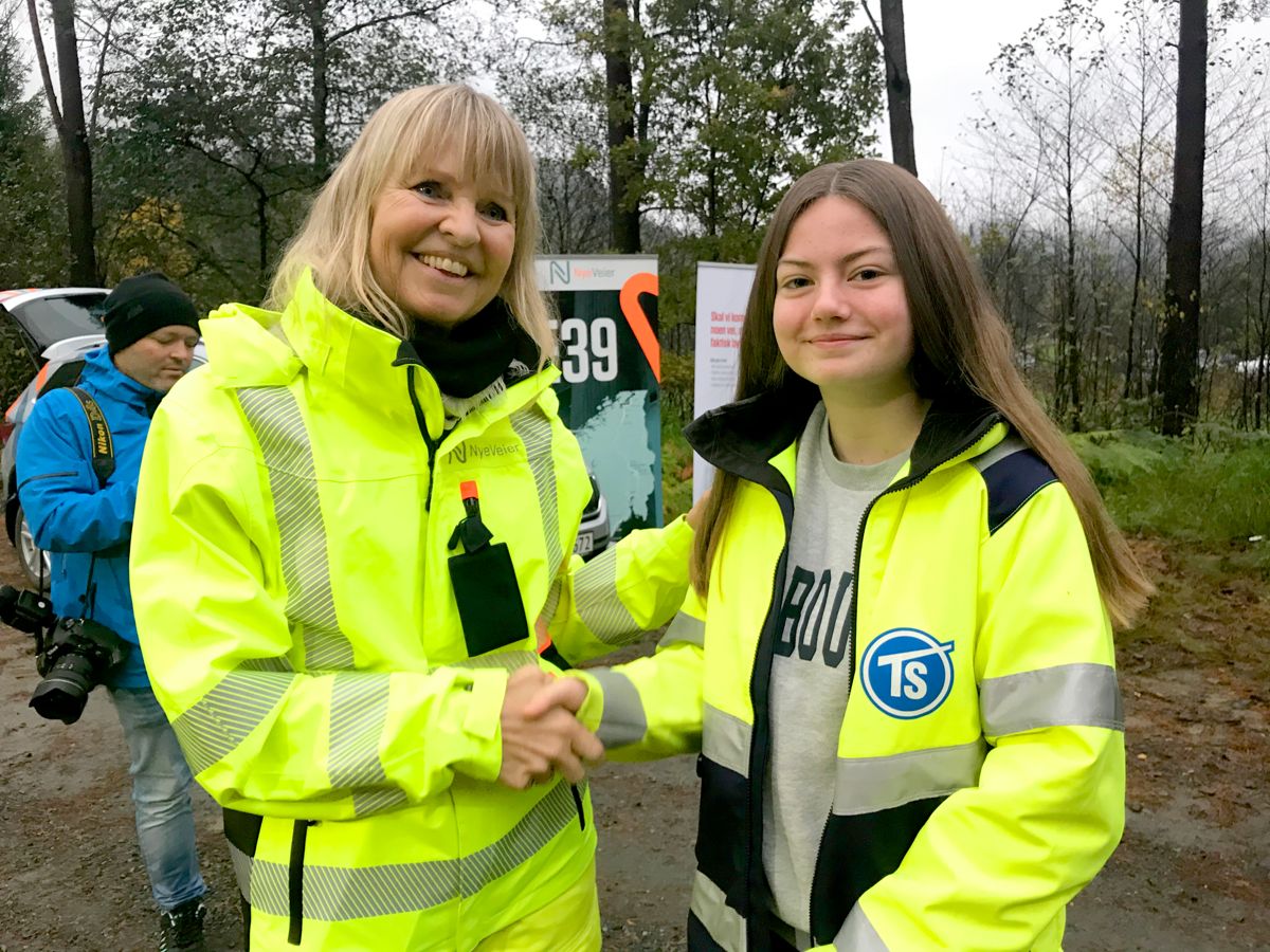 9. klassingen Henriette Omland Andersen (14) fikk æren av å ta aller første gravestikk i prosjektet. Målet er at hun kommer tilbake om fire år og som fersk sjåfør er først til å kjøre på veien. Her gratuleres hun av Nye Veiers administrerende direktør Anette Aanesland.