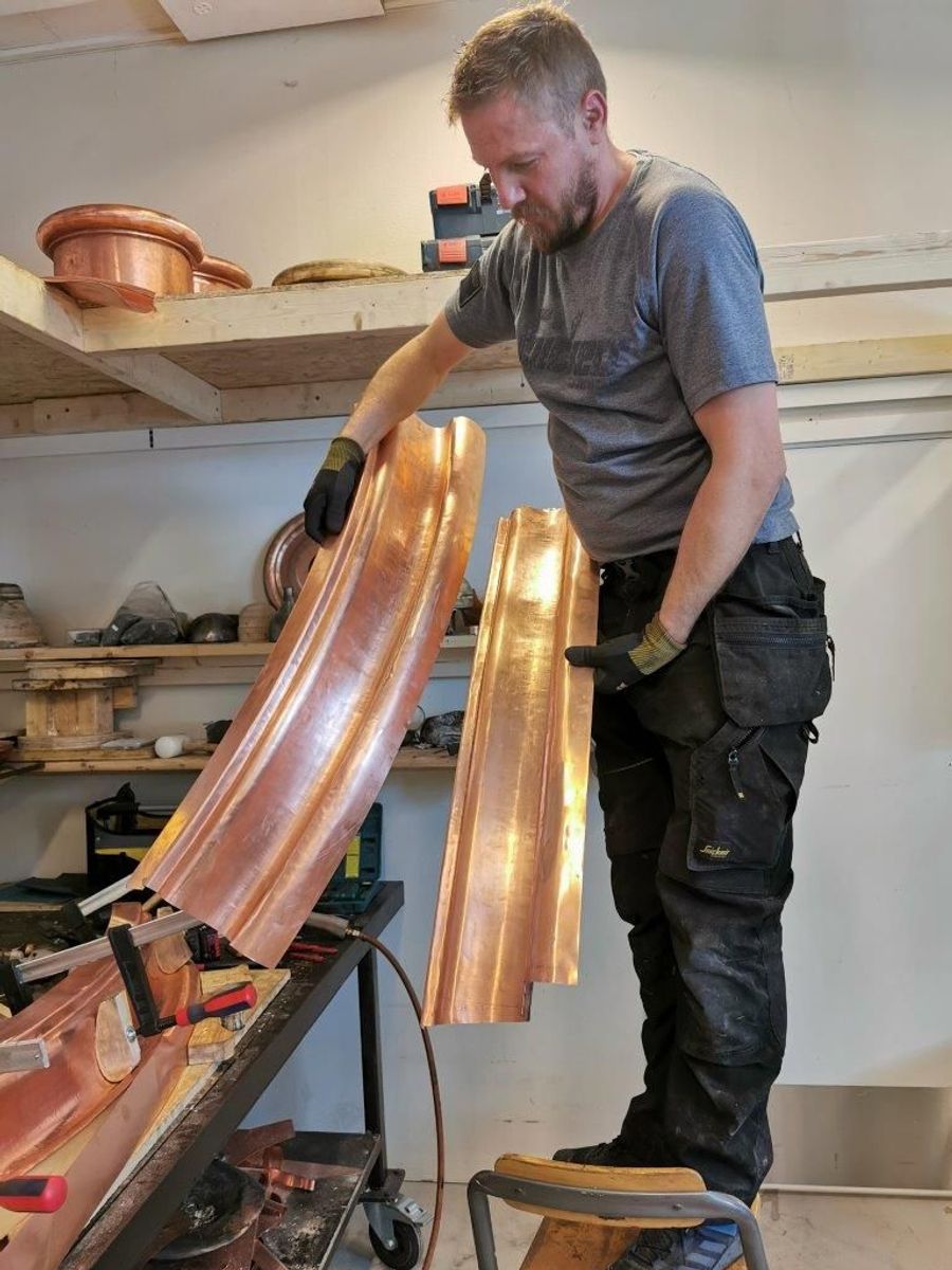 Blikkenslager Gregorz Reichel har hamret ut gesimser i kobber som er formet ut i fra sjablonger av tre kledd med polyetylen. Foto: Karlsen & Nordseth
