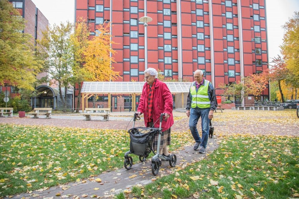 TRIO: Anne, Harald, og katten Daja. Anne går på stien som er tilpasset rullatorbredde. Selve rullatorløypa er rundt hundre meter.I bakgrunnen er blokken hvor de begge bor. Benkene skal få nye armlener, så det blir lettere å reise seg opp. Foto: Fredrik Naumann/Felix Features