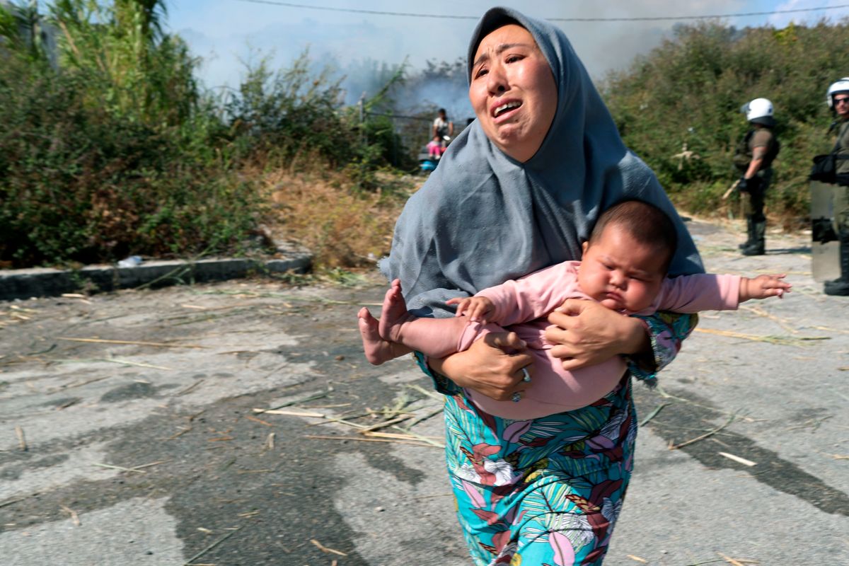 En migrant holder babyen idet hun løper for å unngå en liten brann nær Mytilene på øya Lesbos. Nå åpner Flekkefjord-ordføreren for å ta imot Moria-migranter.