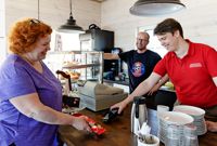 Tuula Åminne köper en glass i kaféet i den nya servicebyggnaden vid gästbåtshamnen på Skeppsbron i Lovisa. Sonen Rasmus Åminne tar betalt. I bakgrunden står hamnkapten Niclas Mattsson.