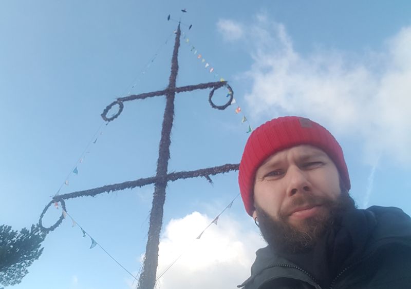 John Björkman bredvid en midsommarstång i Hitis på Kimitoön. Under årets midsommar behövs ingen mössa.