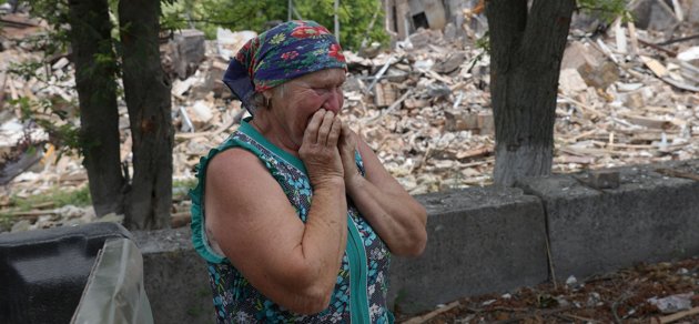 Ukrainska Raisa står bredvid en förstörd skola i byn Bilogorivka i mitten av juni 2022.