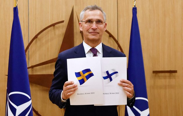 Natos generalsekreterare Jens Stoltenberg poserar med Finland och Sveriges underskrivna Natoansökningar den 18 maj.
