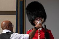 En polis ger vatten till en soldat i vaktstyrkan utanför Buckingham Palace i London på måndagen.