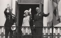 Soligt på slottsbalkongen. President Kekkonen drar undan flaggan som i den okynniga majvinden gjorde sitt bästa att dölja drottning Elisabets och prins Philips vänliga vinkningar. 