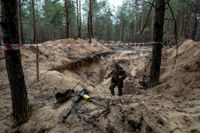 En ukrainsk soldat använder en metaldetektor när han undersöker en massgrav i Izium.
