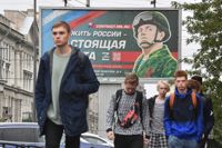 Unga personer promenerar framför en skylt som gör reklam för kontraktbaserad militärtjänstgöring i St:Petersburg den 29 september. På skylten står det "att tjäna Ryssland är ett riktigt jobb". 