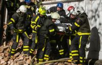 Brandmän bär i väg en person som hittades i rasmassorna efter attacker mot Kiev på måndagsmorgonen.