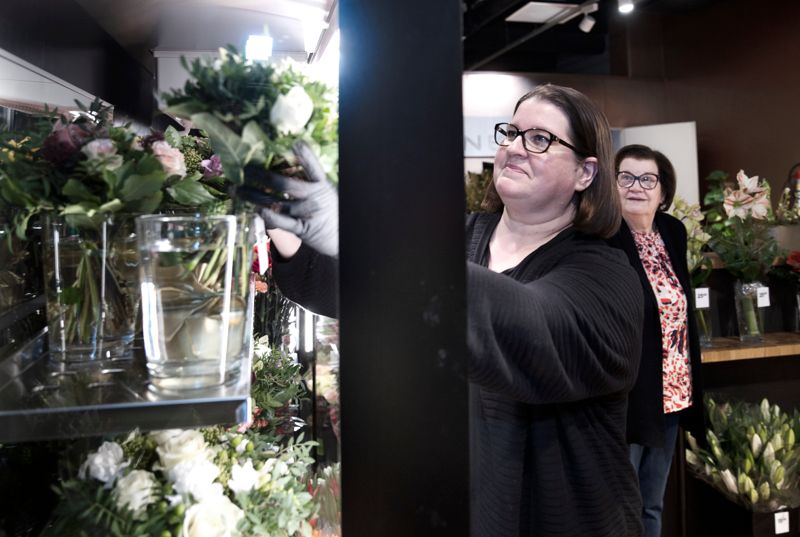 Jonna Mathisen ser till att det alltid finns några färdiga blombuketter bundna i vitrinskåpet. Bland rosor och nejlikor skymtar stjälkar av grevillea och vinterbär (skimmia). I bakgrunden syns ”säsongsbiträdet” Leena Markkanen.