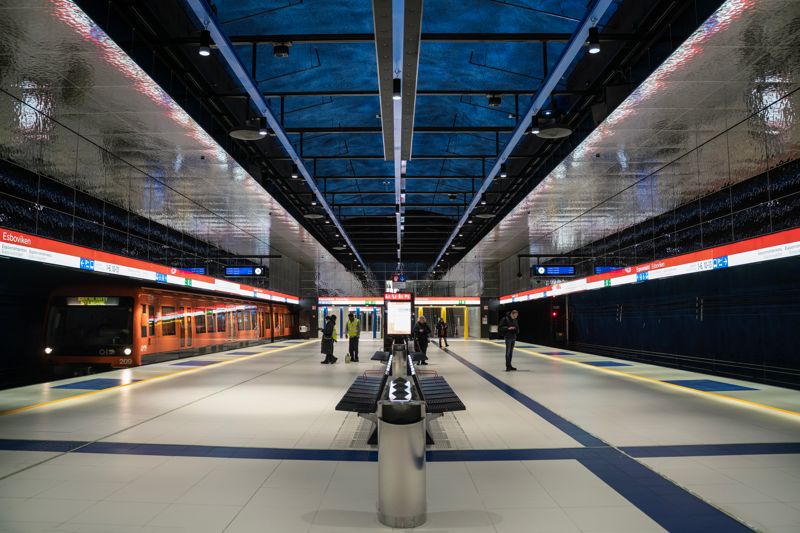 Hans Rosenströms ljus- och ljudverk ”Skuggor på ytan” syns i taket på Esbovikens hållplats. Metrovagnar och människor som passerar förbi reflekteras också i de metalliska plattorna som hänger på väggarna. Stefan Lindfors är imponerad av verket.