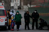 Kinesisk polis kontrollerar en man som vilar på sitt bagage i Peking under fredagen.