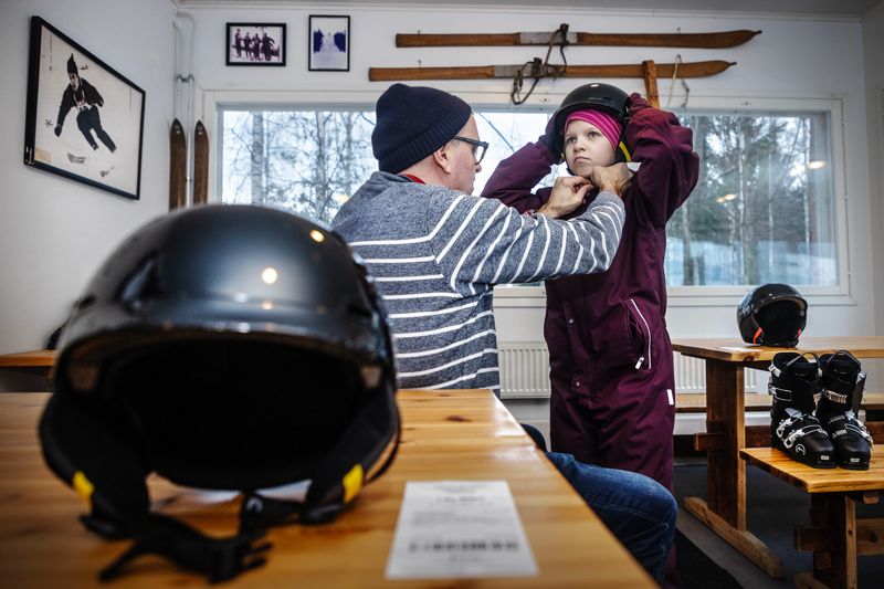 Pappa Klas Ljungberg hjälper 10-åriga Martha Honkavuo med hjälmen inne i kaféet där skoleleverna byter om till skidutrustning innan slalomklubben börjar.