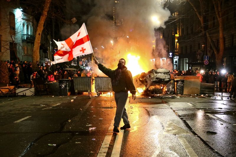 En man med den georgiska flaggan framför en brinnande barrikad i närheten av parlamentet i Tbilisi under veckans protester.