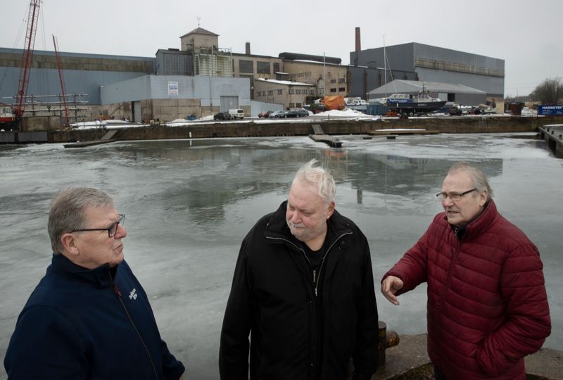 Esko Antikainen, Tomy Wass och Kauko Pentikäinen står i hamnen framför tidigare FN Steel, nu en marina.