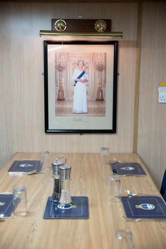 I mässen finns ett porträtt på drottning Elizabeth II som den nu bortgångna drottningen själv signerat bilden 2001 när fartyget togs i bruk.På motsatt vägg finns också ett porträtt på fartygets sponsor, prinsessan Anne. – Hon brukar besöka oss ungefär en gång om året. När fartyget får en bild av nykrönte kung Charles III återstår att se, konstaterar Chris Jones men han är uppenbart stolt över bilderna.