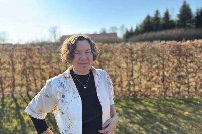 Eva Moth Andersen i sin have. Bag hende kan man lige ane tårnet af Hørup Kirke. Det er i kirkecentret ved siden af kirken, at kvinder mødes til »Delemad og Dybde«.