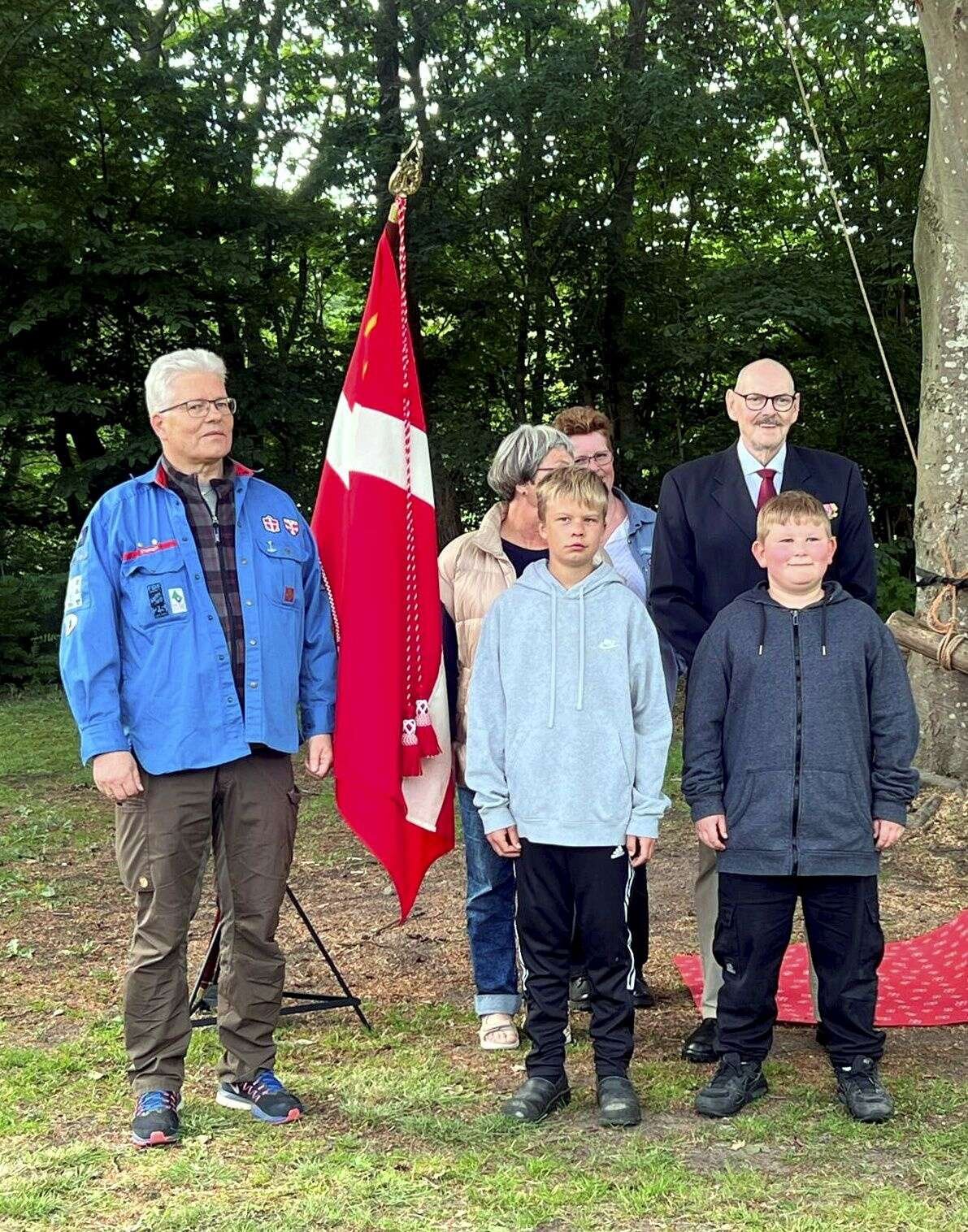 Preben Kvist (tv) har været medlem af FDF Stoholm i næsten 60 år og fik lov at slå det tredje søm i fanen, som Andreas og Albert i forgrunden satte i holderen. Formand for Dannebrogs-Samfundets Skive-afdeling Preben Sloht (th) slog det første i, mens sognepræst Anna-Christine Elming (i midten) svang hammeren på nummer to. Bagerst anes kredsleder Jette Boe. Privatfoto