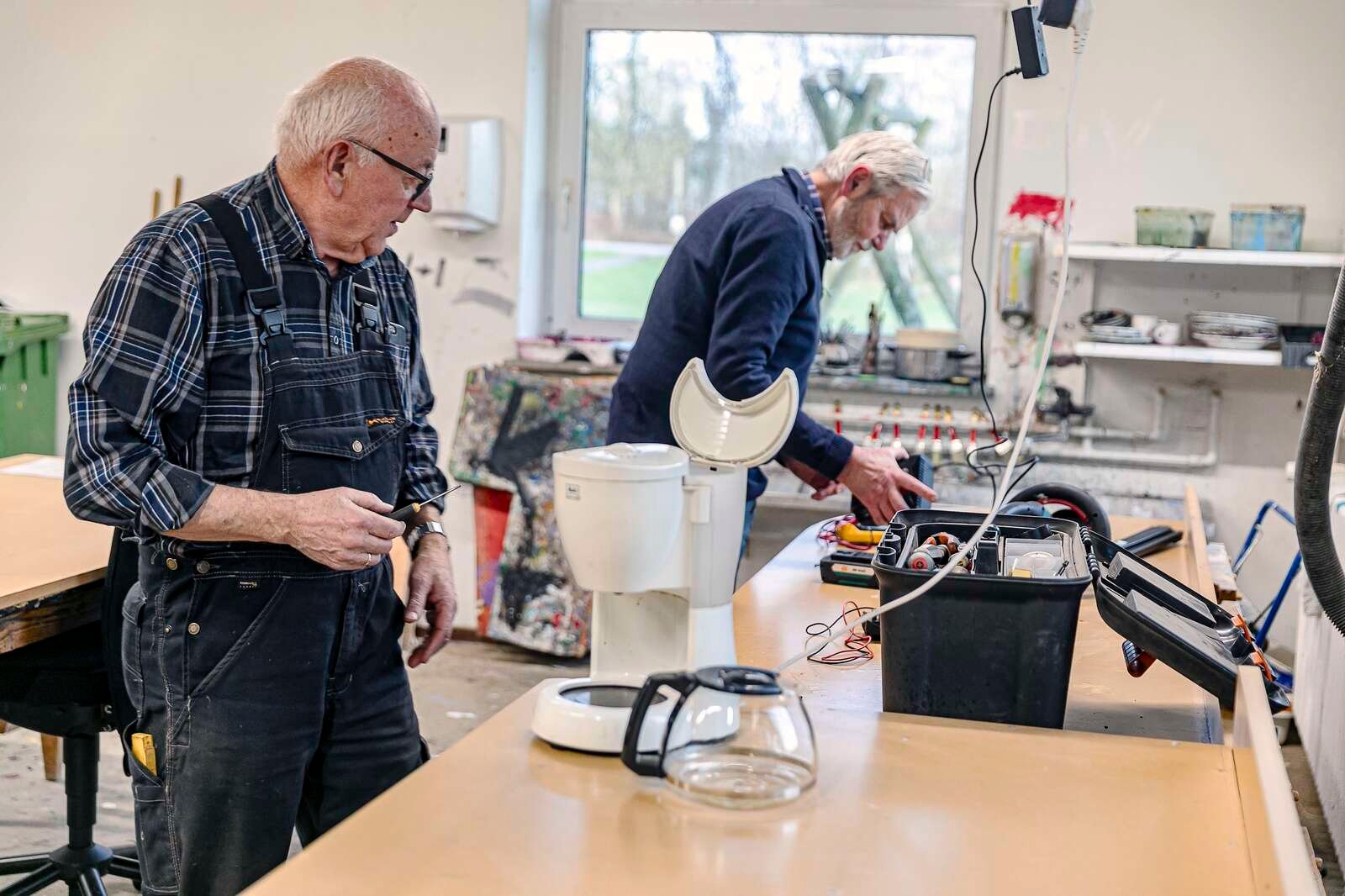 Ejner Tranberg træder til og fikser en kaffemaskine, når bønner ikke længere hjælper. I baggrunden er Niels Vendelbo gået løs på en hækkeklipper.