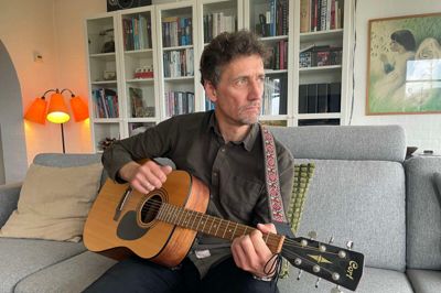 Søren Bech med drømmende blik og guitaren i hånden hjemme i dagligstuen i Resen. Foto: Jan la Cour