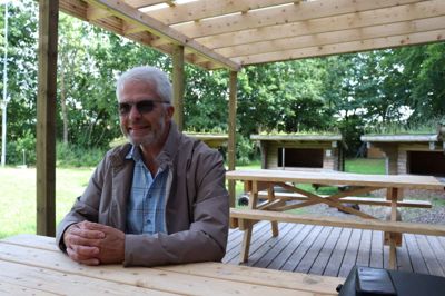 Formanden for FDF i Isenvad, Bent Bækgaard, har taget plads på det overdækkede plateau ved pavillonen, der er blevet til ved hjælp af gode, frivillige kræfter og godt forældre-sammenhold i kredsen.