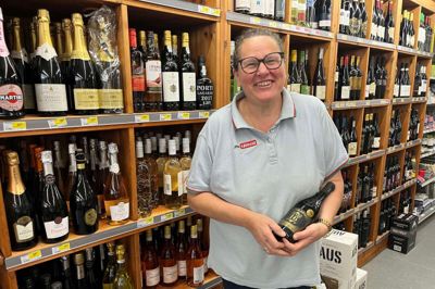 Købmand Jette Steffensen med en af de vine, der bydes på, når der i ugens løb er vinsmagning i forbindelse med jubilæet. Til vinsmagning kommer Birte Mørrup og dele smagsprøver ud. Hun er nemlig også en af de frivillige i butikken.
