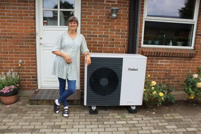 Laila Simonsen ved varmepumpeanlæg foran huset. Jep, det ligner en kummefryser, men det kan afskærmes lidt.
