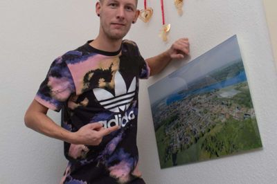 Jakob Mikkelsen har siden 2019 boet i lejlighed i Flensborg. Her sidder han i sit køkken med fødebyen Ans hængende på væggen. Foto: Jakob Mikkelsen
