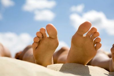 Close-up of two soles of human sunbathing on sandy beach