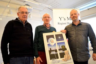 Svend Erik Falkesgaard (tv.) og Ejner Andersen fra Julemærkeudvalget hos Fonnesbæk Y's Men's Club fremviser årets julemærke i selskab med René Kjær, der har kreeret motivet "Et lys i mørket"