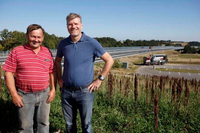 Fabrikschef Poul Jakobsen (t.v.) og salgschef Michael Pedersen. På samkøringspladsden holder Svend Aage Nielsen i sin betonkanon, og i baggrunden ses en af de mange motorvejsbroer, som »hans« samt firmaets andre 126 betonkanoner har leveret beton til. ?Foto: Jens Anton Nordestgaard