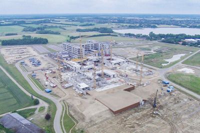 Et vue over hospitalsbyggepladsen i Gødstrup, taget med den drone, der har leveret optagelser til videoen. Området, hvor servicebyens godt 6000 kvadratmeter skal opføres, ligger i forgrunden foran helikopterlandspladsen, og lidt for sig selv yderst til højre ses fundamentet til kapellet, der i mellemtiden er begyndt at skyde op. ?Foto: Region Midtjylland