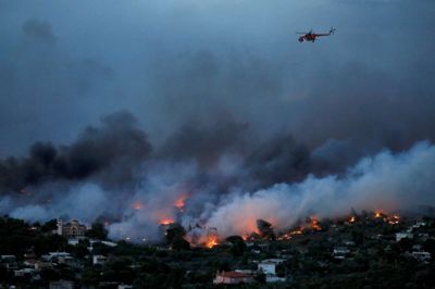 En helikopter, der deltager i slukningsarbejdet, flyver over en brand i byen Rafina i Grækenland. Foto: Alkis Konstantinidis/Reuters