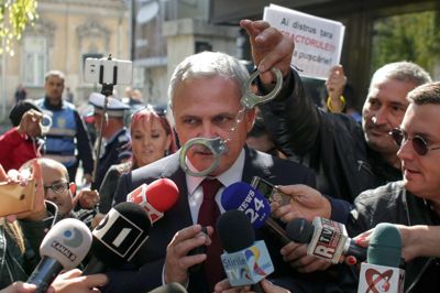Inquam Photos/Reuters. En demonstrant vifter med et sæt håndjern foran den rumænske toppolitiker Liviu Dragnea i Bukarest. Lederen af Rumæniens regerende socialdemokrater indledte mandag afsoningen af en fængselsstraf på tre og et halvt år, efter at landets højesteret havde opretholdt en dom til ham for politisk korruption.