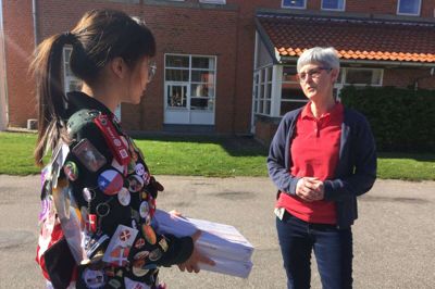 I den legendariske Rotary jakke, der er tom, når man rejser ud, men efterhånden bliver fyldt med minder, venskaber og souvenirs fra udvekslingsåret, overrækker Janet Chin Tang to kasser mundbind til den ansvarlige i Ikast-Brande Kommune, Margit Andersen. Foto: Laila Kempel