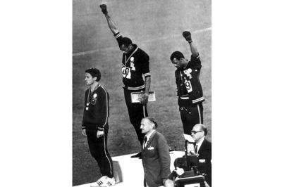 Med bøjede hoveder og hver sin handskeklædte hånd knyttet mod himlen demonstrerede de to sprintere Tommie Smith (i midten) og John Carlos (til højre) mod det amerikanske samfunds behandling af sorte borgere. Det skete under afspilningen af nationalmelodien ved OL i Mexico i 1968.