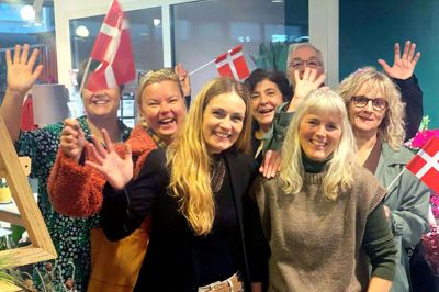 Vibeke Søgaard forrest til højre blev tirsdag morgen overrasket af sine kolleger, der stod klar med flag, morgenkaffe, gaver og lykønskninger. I 25 år har Vibeke Søgaard bundet blomster til Ikasts borgere fra Rex Blomster i Strøgcentret. Foto: Anne Dalsgaard