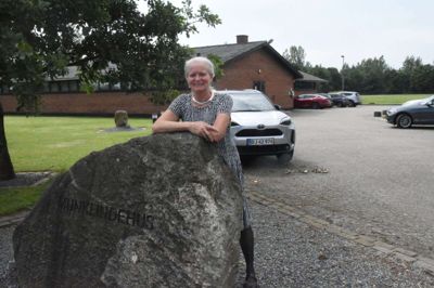 Formanden for Munklindehus udenfor det jubilerende forsamlingshus. Kirsten Jensens største jubilæumsønske er et nyt tag.