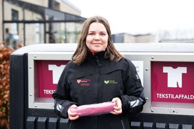 Freja Slothuus Hørning fra Ikast-Brande Kommune ses her foran en af de genanvendte affalds-kuber, der nu skal rumme tekstilaffald. I løbet af foråret vil alle husstande også modtage røde poser som en opfordring til at sortere tekstil-affald fra det øvrige affald. Foto: Linna Grøn