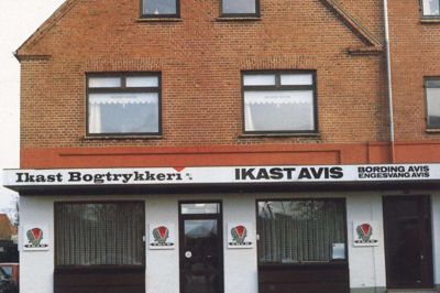 Fra nummer 59 til nummer 40 i den gade, som ved avisens etablering hed Bredgade, og i dag hedder Strøget, flyttede Ikast Avis i begyndelsen af 1930’erne, formentlig 1932. Efter en renovering i 1982 tog facaden sig således ud med tydelig skiltning af avis og bogtrykkeri og med springvand i forgrunden. Foto: Arkiv