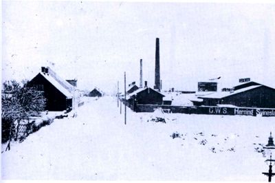 C.W.S.-navnet er tydeligt på dette billede af Herning Svineslagteri fra vinteren 1912-1913. Billedet er taget fra Fonnesbechsgade (bemærk gaslygten i højre hjørne) og viser Slagterivej - den senere og nu stort set forsvundne Poulsgade - med slagteriet og enkelte énfamiliehuse. ? Foto fra »Slagteri i Herning gennem 100 år«.