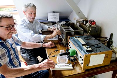 Bemærk ølflasken til højre. En kort men uendelig båndstrimmel med et morsesignal kører i ring fra spolebåndoptageren og rundt om flasken. Tanken er at signalet sendes fra radioen mod en meteorsværm, der så spejler det ned til en anden radioamatør på kloden. Poul Erik Skov (OZ9PZ) og Niels Erik Mikkelsen (OZ2ND) demonstrerer. ?foto: jørn deleuran