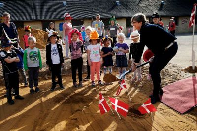 Dorte West, formand for børne- og familieudvalget, tog det første spadestik i går eftermiddag, mens børnene fra indskolingen - nogle af dem iklædt sjove hatte - kiggede på. Bagefter fik de selv lov at grave lidt. ?foto: Flemming Hansen