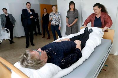 Ergoterapeuterne Christina Hjelm Jakobsen og Helle Fjederholt Espersen bruger distriksleder Åse Jonassen som testperson til at fremvise deres »kropsafgrænsende lejringsmetode«. Imens kigger innovationsminister Sophie Løhde og borgmester Lars Krarup til. ? Foto: Henrik Ole Jensen