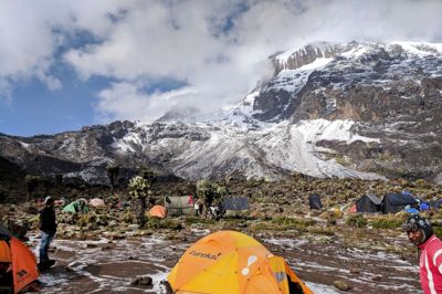 Vores telt i campen, hvorfra vi kan kigge op mod den tinde, vi skal bestige om kun halvanden dag. Til højre er vores chefguide, Dismas. Den anden guide hed God Listens. Foto: Bjarne Gregersen