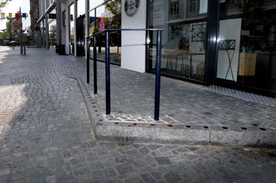 Fire butikker har fået en rampe og et trappetrin som en del af gågaderenoveringen, men dem er rigtig mange borgere faldet i. Et gelænder er kommet op, og i åbningstiden stiller butikkerne gadevarer rundt om, men det har ikke fjernet problemet. ? Foto: Henrik Ole Jensen